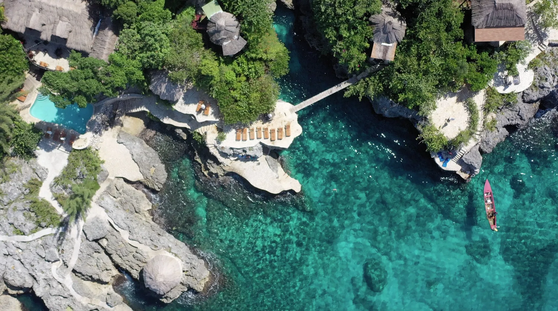 Aerial view of cliffside coves, loungers, thatched roofs, and turquoise water at Tensing Pen Hotel.