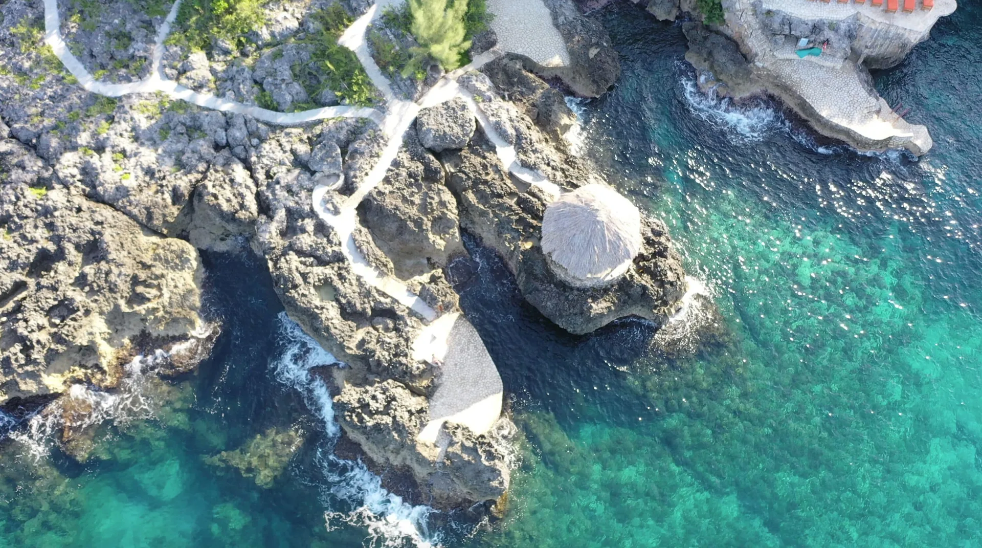 Aerial view of rocky cliffs, paths, and turquoise water at Tensing Pen Hotel.