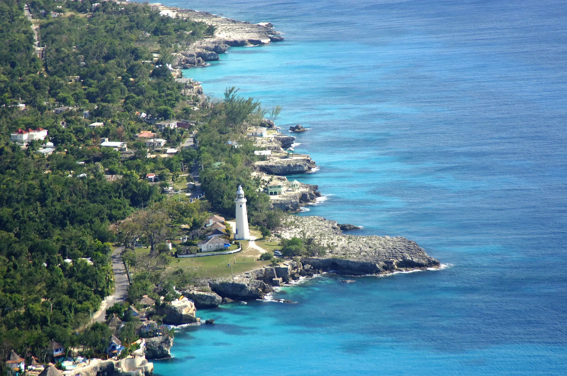 An aerial view shows a lighthouse and turquoise coastline near Tensing Pen Hotel.