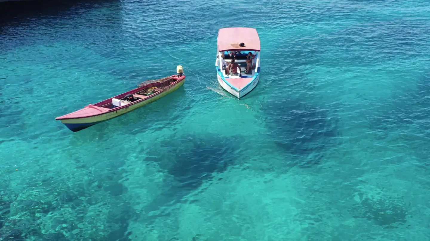 Two small boats float on clear turquoise water near Tensing Pen Hotel.