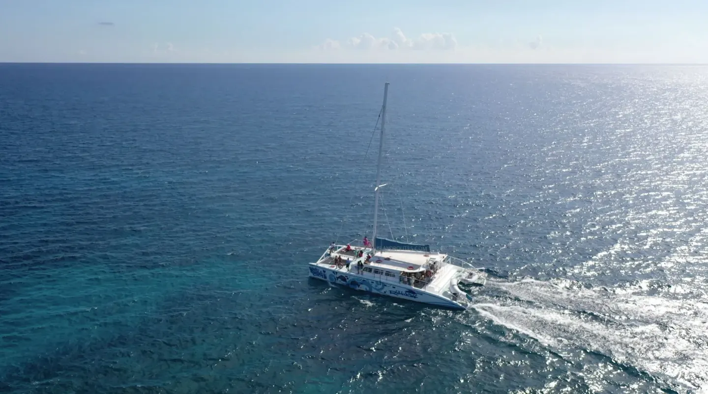 A catamaran sails across bright blue water near Tensing Pen Hotel.