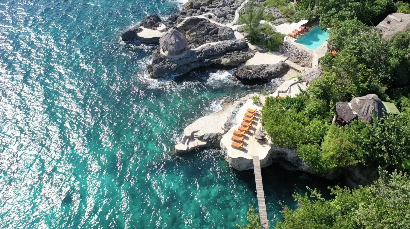 Aerial view of cliffside decks, pool, and turquoise sea at Tensing Pen Hotel.