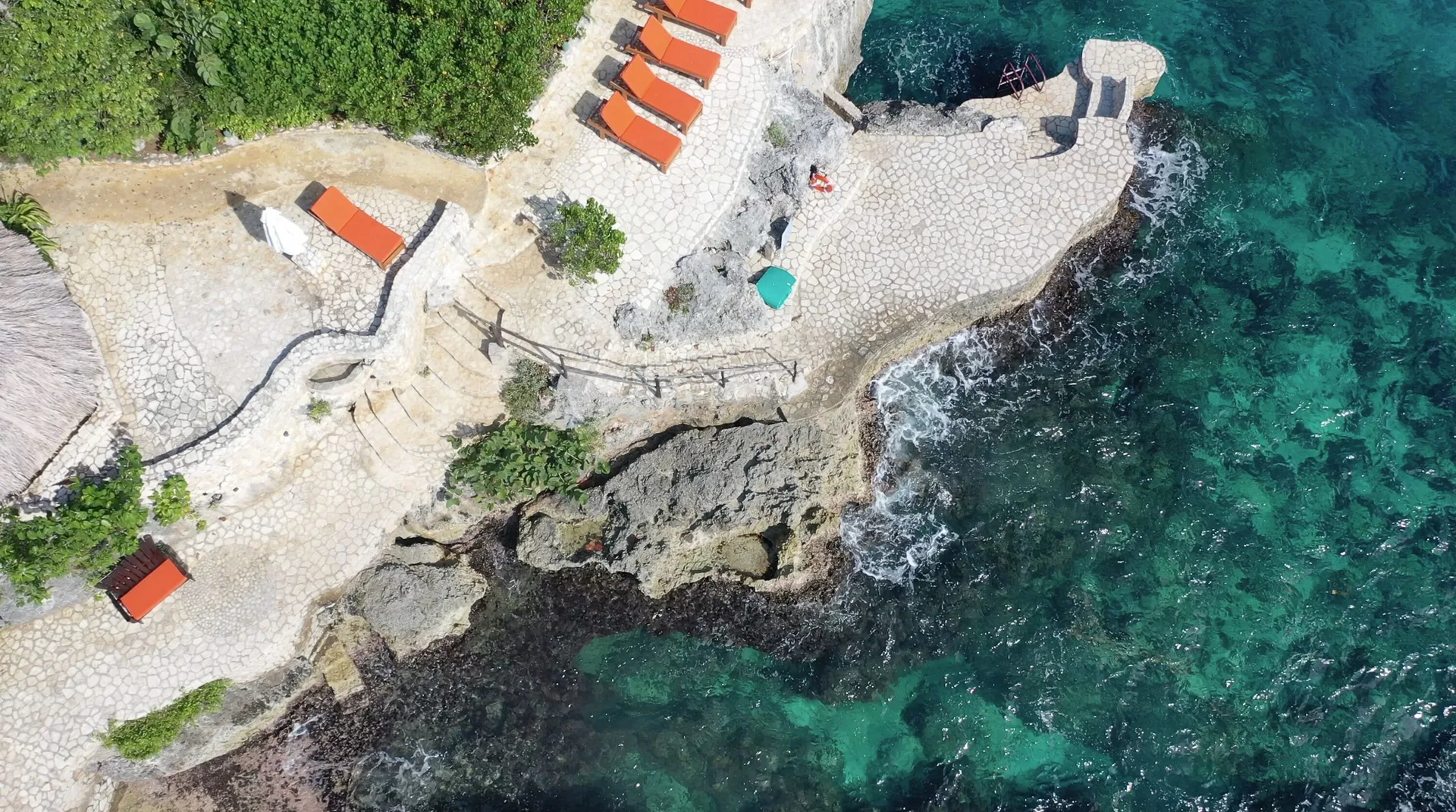 Stone cliff terrace with orange loungers beside clear turquoise sea at Tensing Pen Hotel.