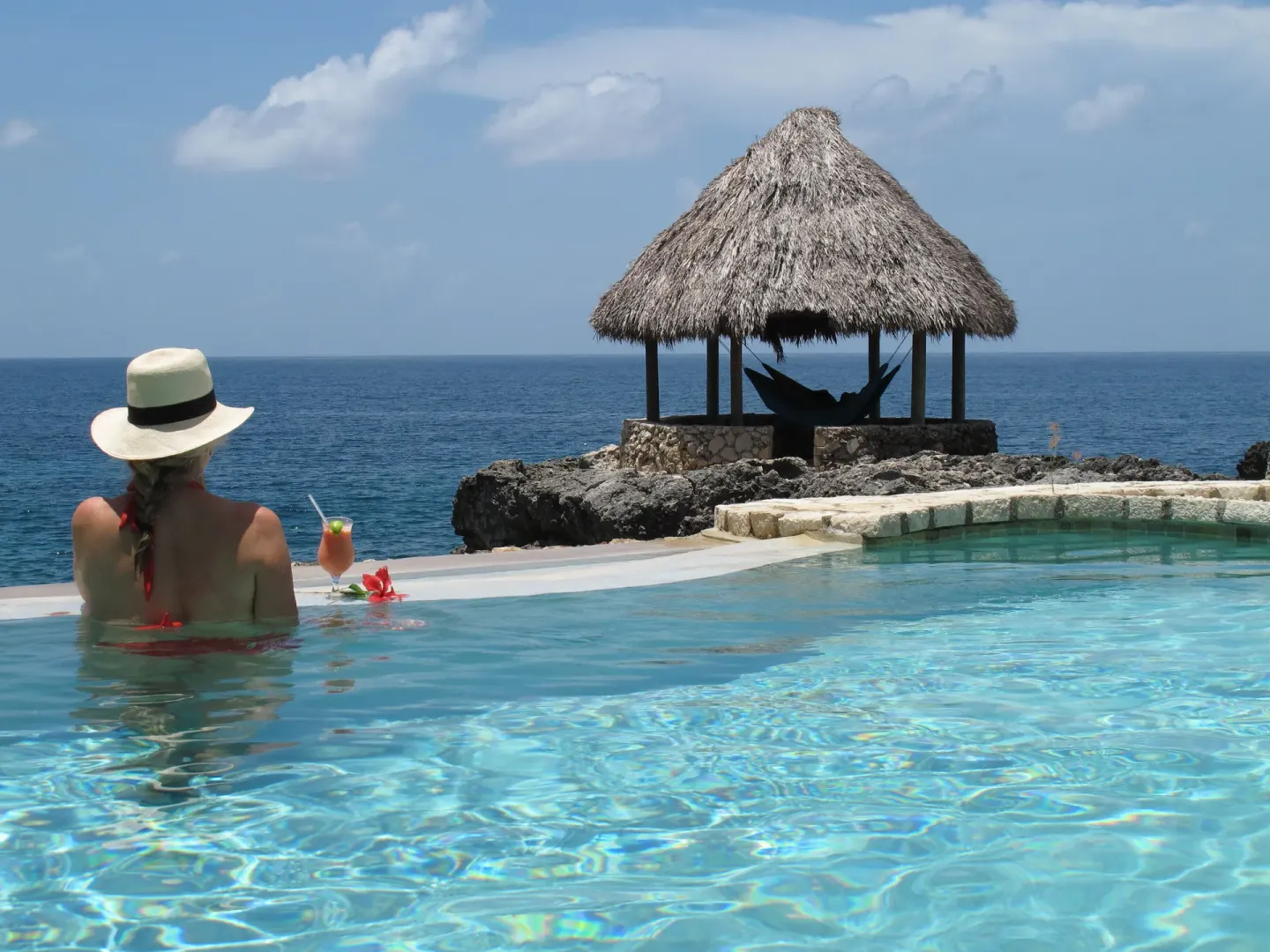 Guest in the pool facing a thatched pavilion and ocean at Tensing Pen Hotel.