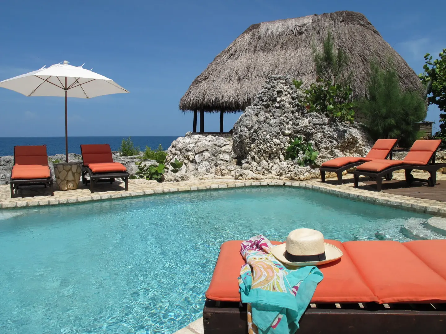 Pool terrace with orange loungers and a thatched pavilion at Tensing Pen Hotel.