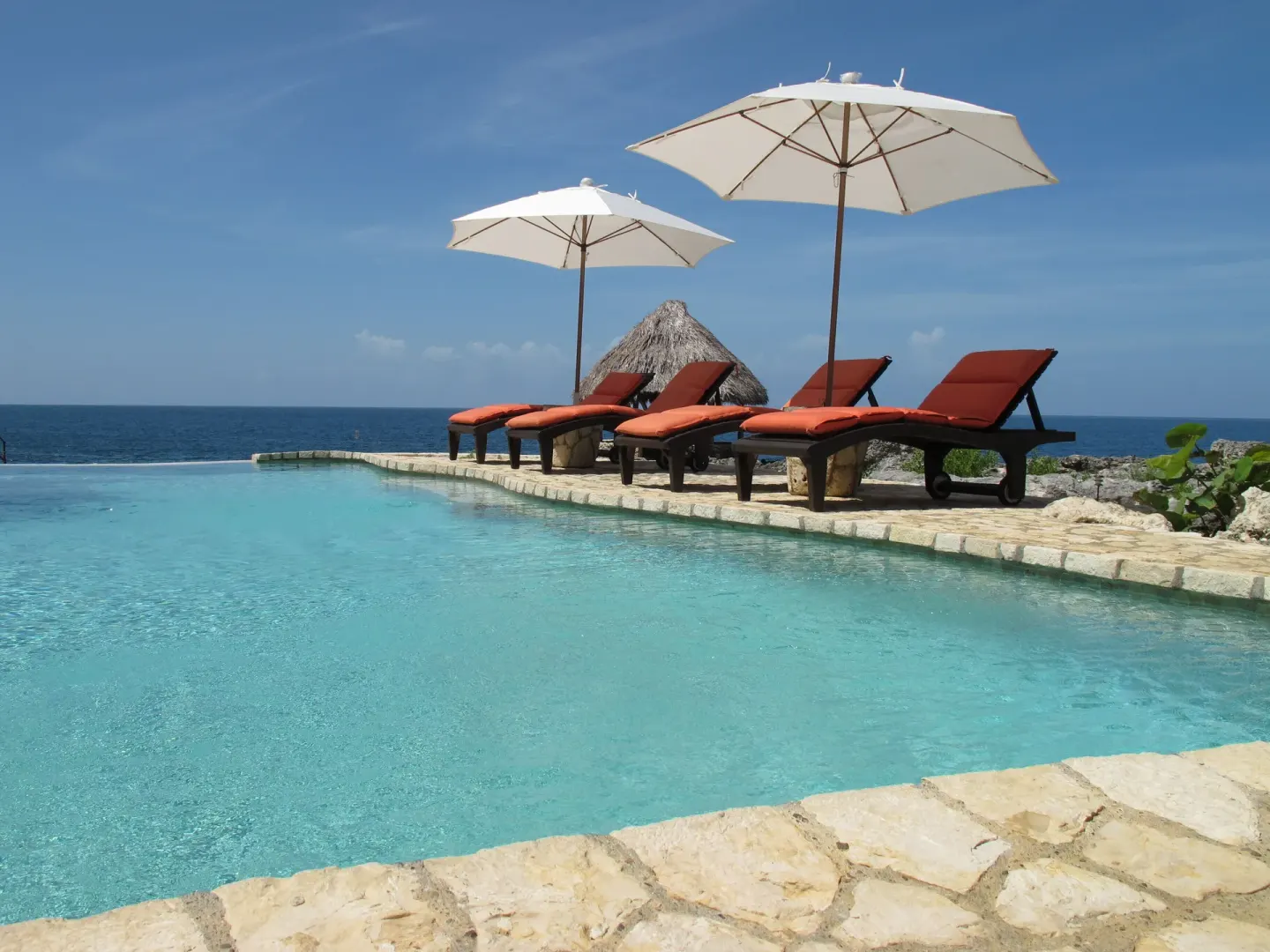 Poolside loungers with white umbrellas overlooking the ocean at Tensing Pen Hotel.