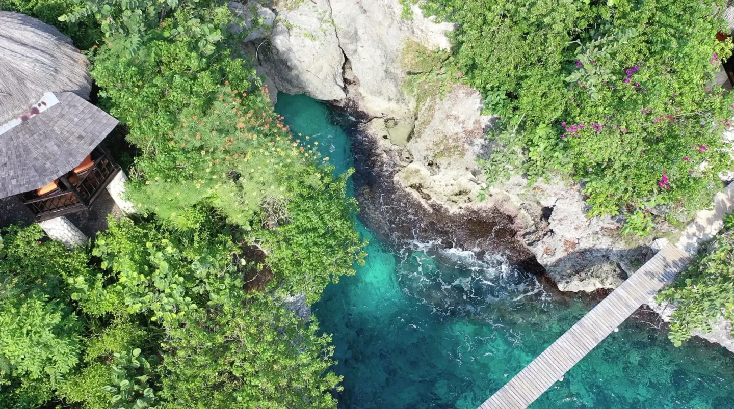 Aerial view of a rocky turquoise cove and footbridge at Tensing Pen Hotel.