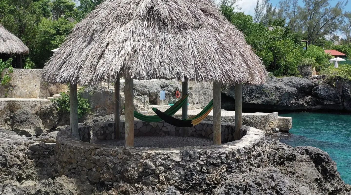 Thatched seaside gazebo with hammocks beside turquoise water at Tensing Pen Hotel.