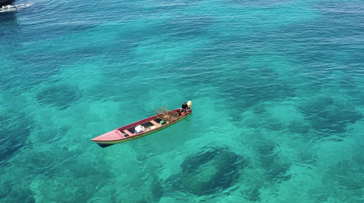 A small wooden boat floats on turquoise water near Tensing Pen Hotel.
