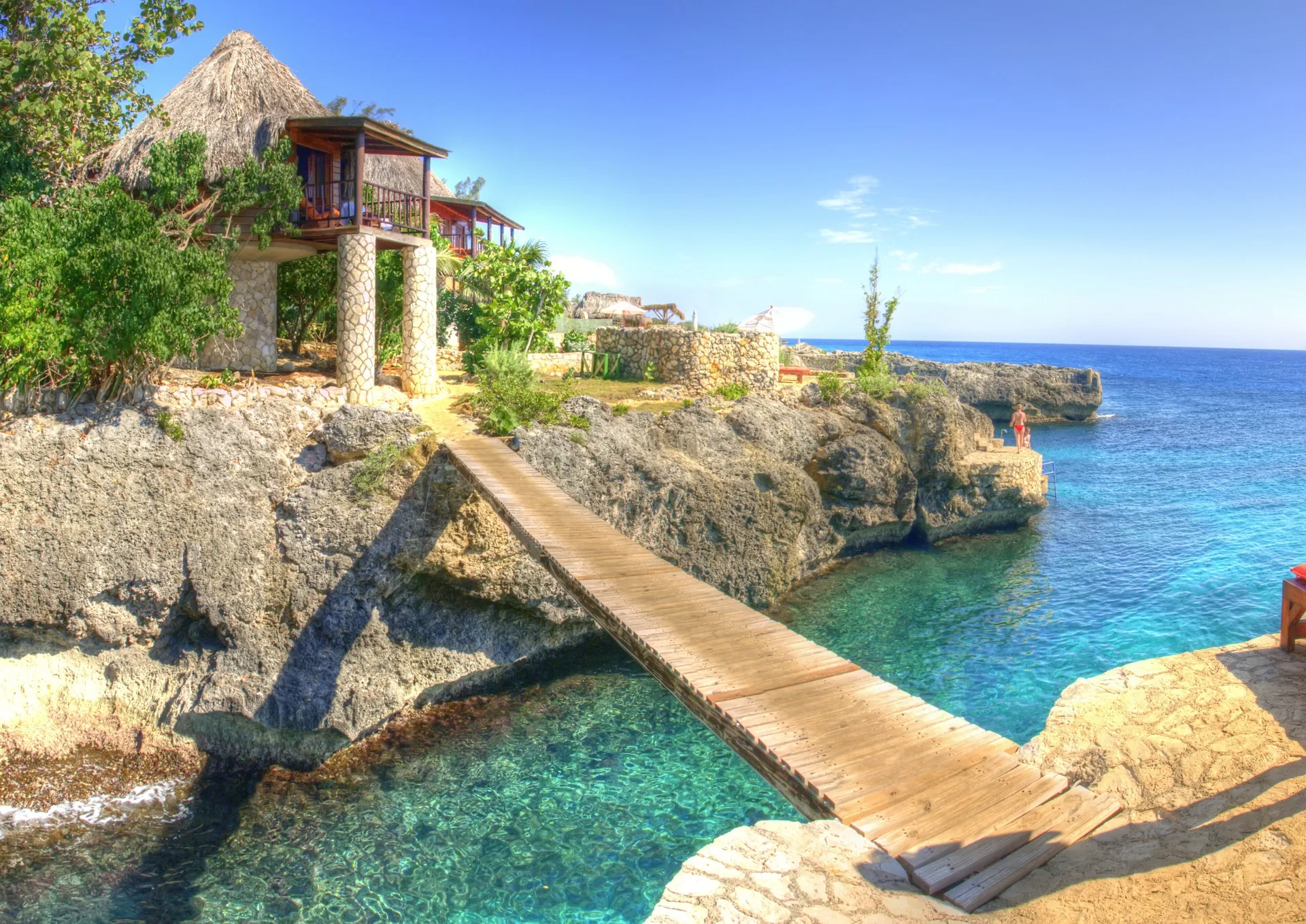 A wooden bridge crosses a clear rocky cove beside cottages at Tensing Pen Hotel.