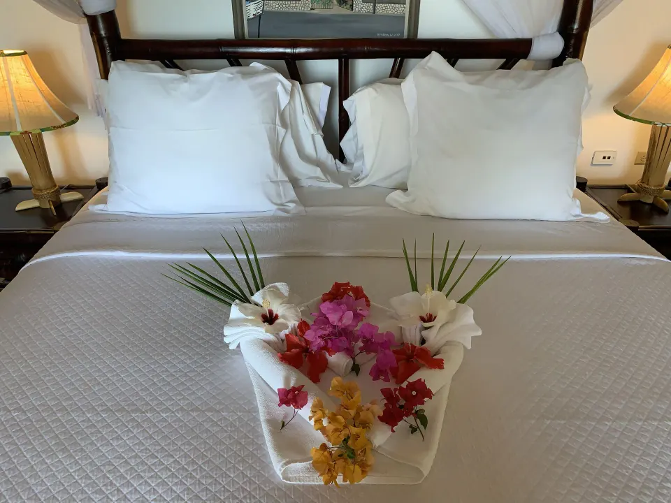 Deluxe Room Ocean View bed close-up with flowers on white linens at Tensing Pen Hotel.