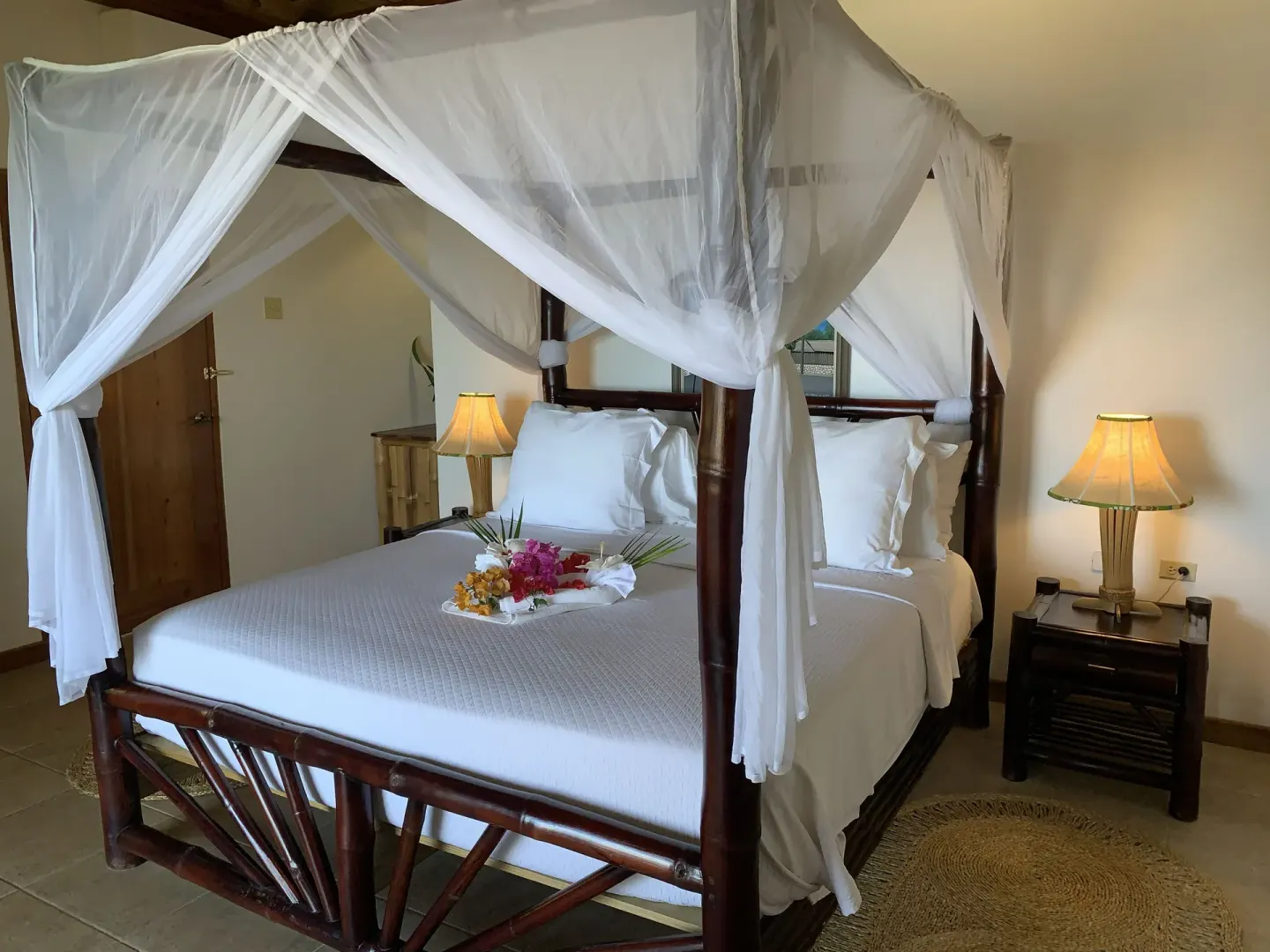 Deluxe Room Ocean View canopy bed with white netting and bedside tables at Tensing Pen Hotel.
