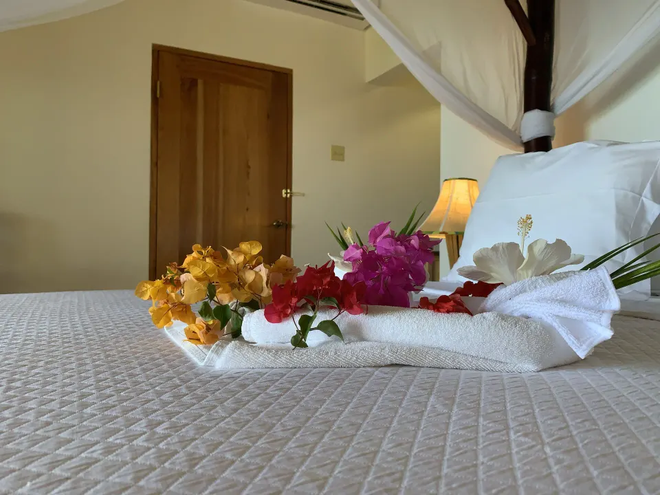 Deluxe Room bed with canopy netting, flowers, and towels at Tensing Pen Hotel.