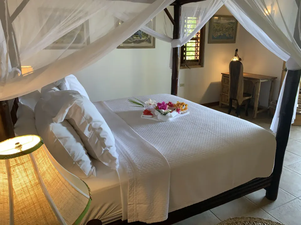 Deluxe Room Ocean View canopy bed with flowers and writing desk at Tensing Pen Hotel.