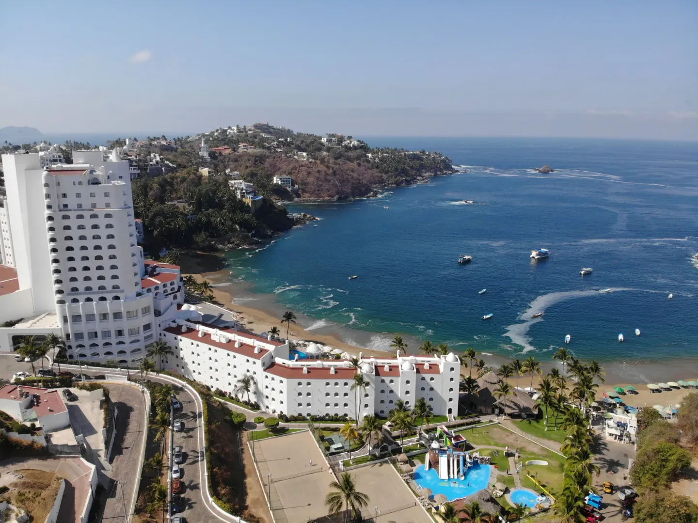 Aerial view of Tesoro Manzanillo beside a blue bay with boats and beach.