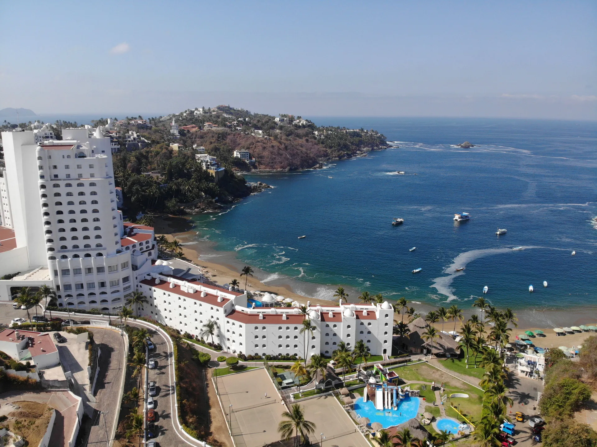 Aerial view of Tesoro Manzanillo beside a blue bay with boats and beach.