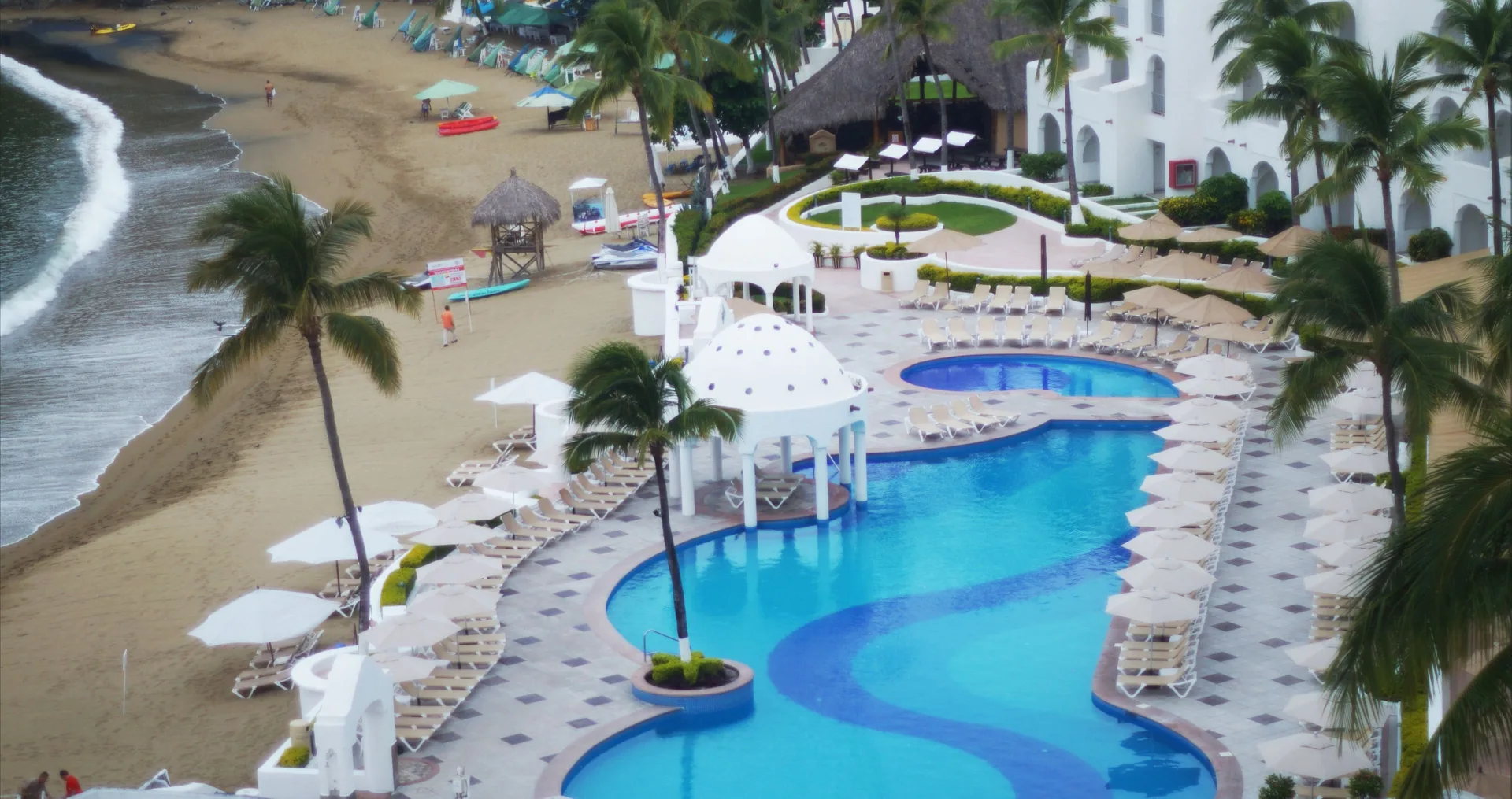 Beachfront pools, loungers, palms, and sandy shore at Tesoro Manzanillo.
