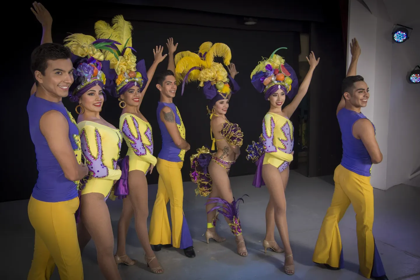 Performers in yellow and purple carnival costumes pose on stage at Tesoro Manzanillo.