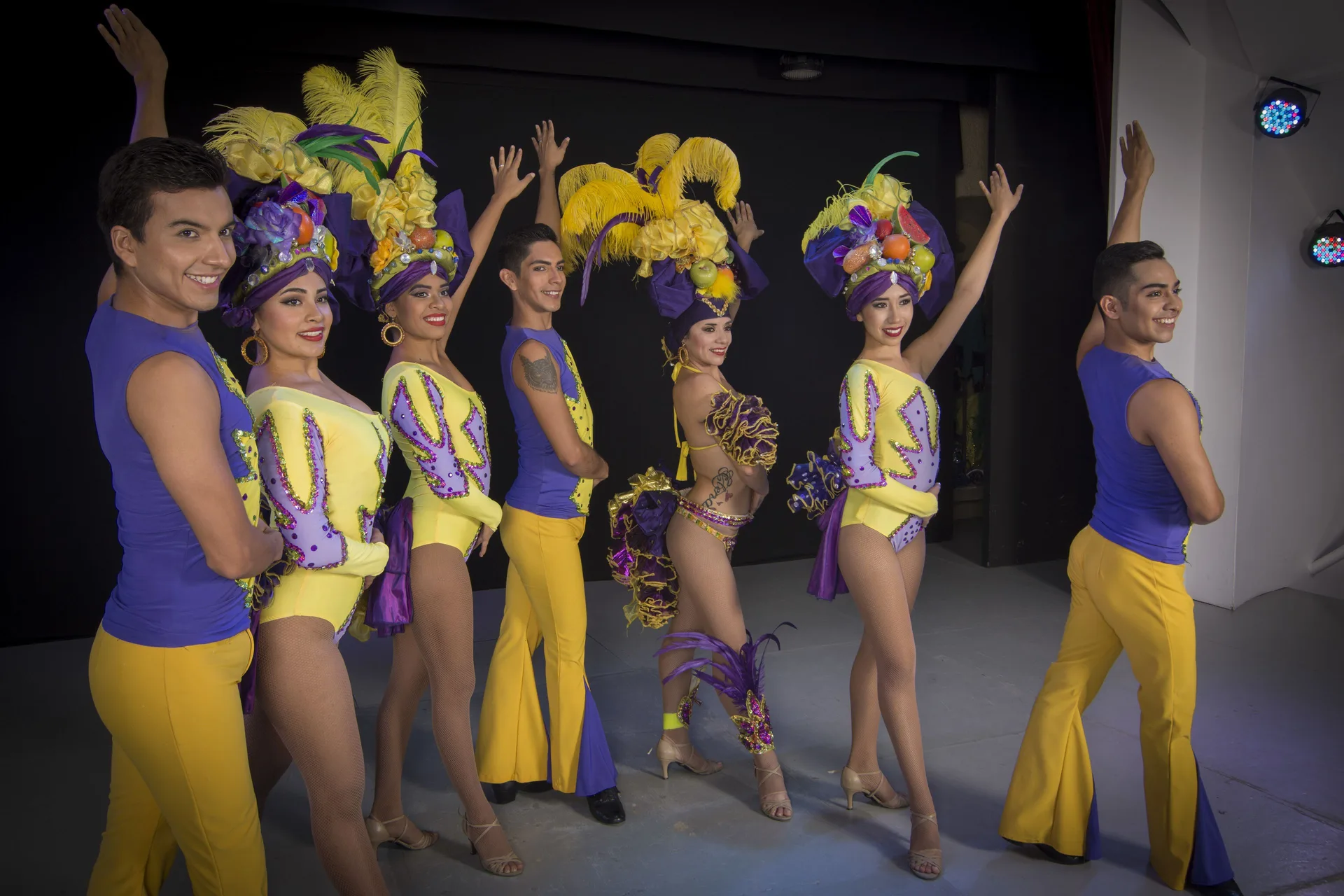 Performers in yellow and purple carnival costumes pose on stage at Tesoro Manzanillo.