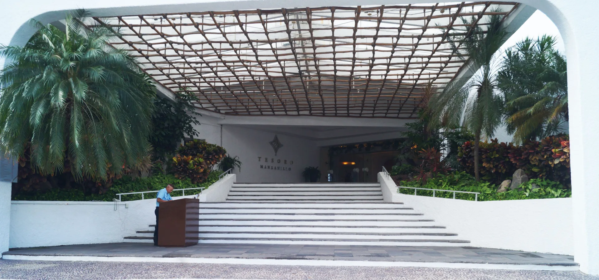 Daytime entrance of Tesoro Manzanillo with wide stairs, palms, and a covered arrival canopy.