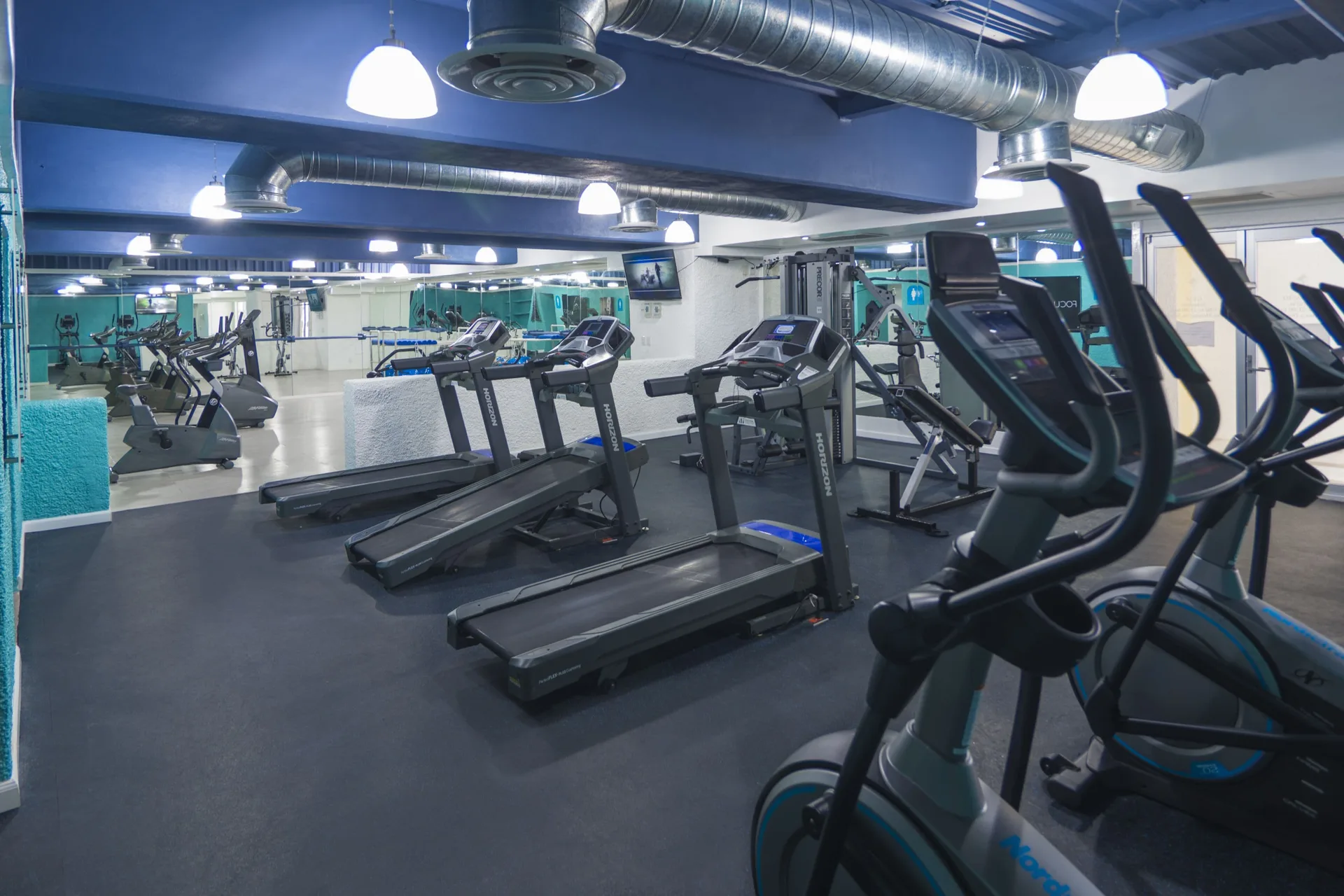Gym with treadmills, ellipticals, mirrors, and exposed ceiling ducts at Tesoro Manzanillo.