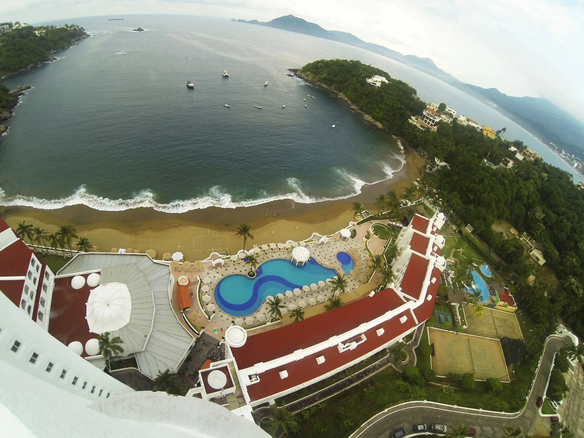 High view from Tesoro Manzanillo over the pool, beach, bay, boats, and green headlands.