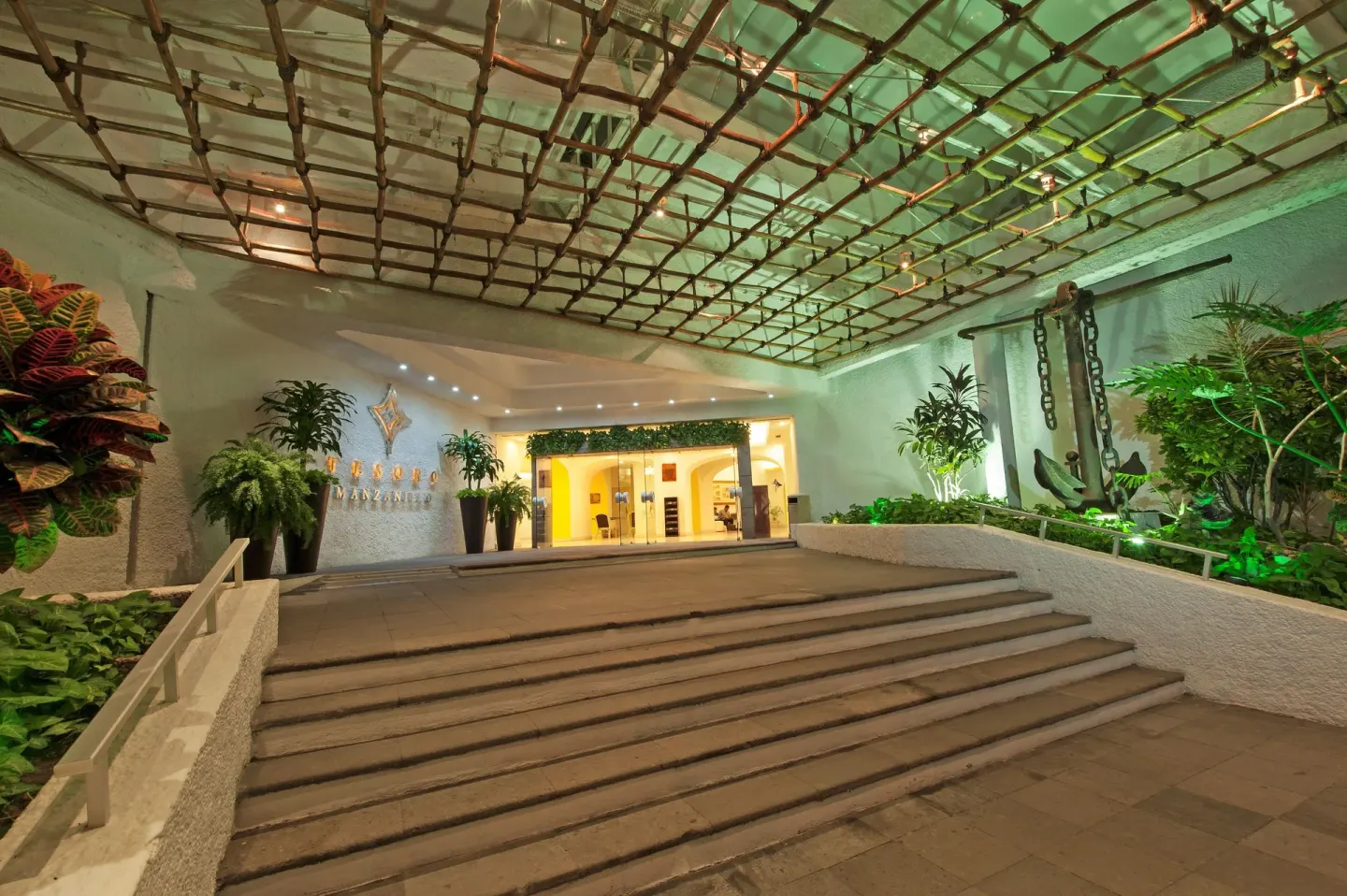 Night entrance of Tesoro Manzanillo with steps, greenery, and a canopy over the arrival area.