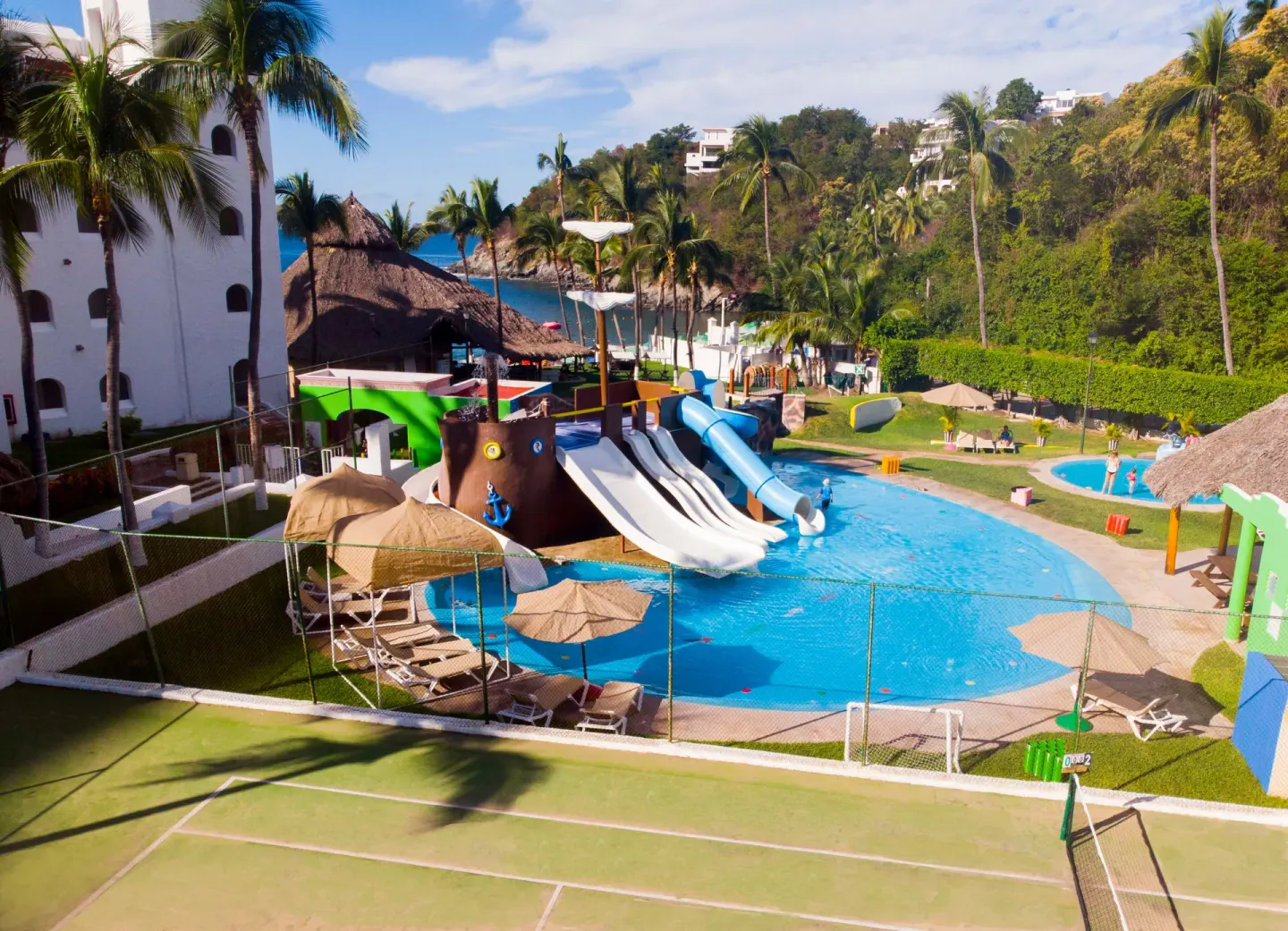 Pool with waterslides, lounge chairs and hillside greenery at Tesoro Manzanillo.