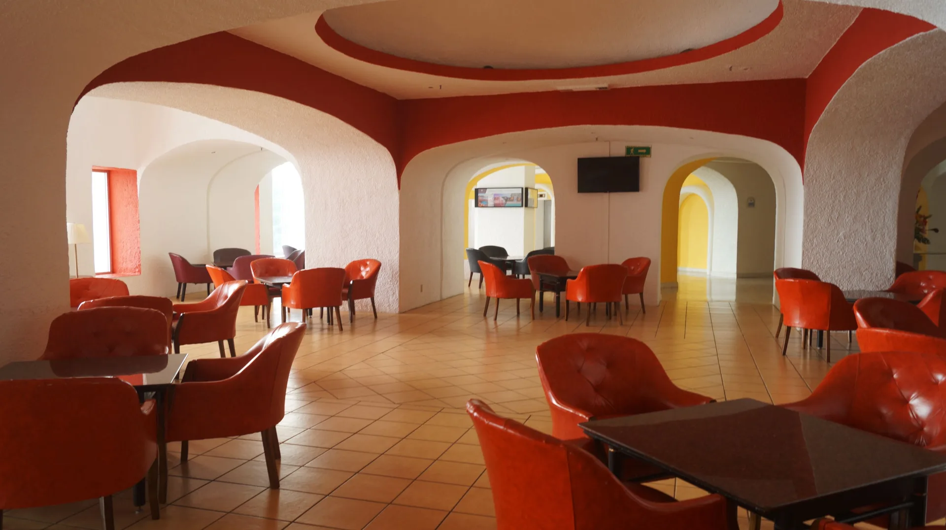 Indoor lounge with red chairs, tables, and arched openings at Tesoro Manzanillo.