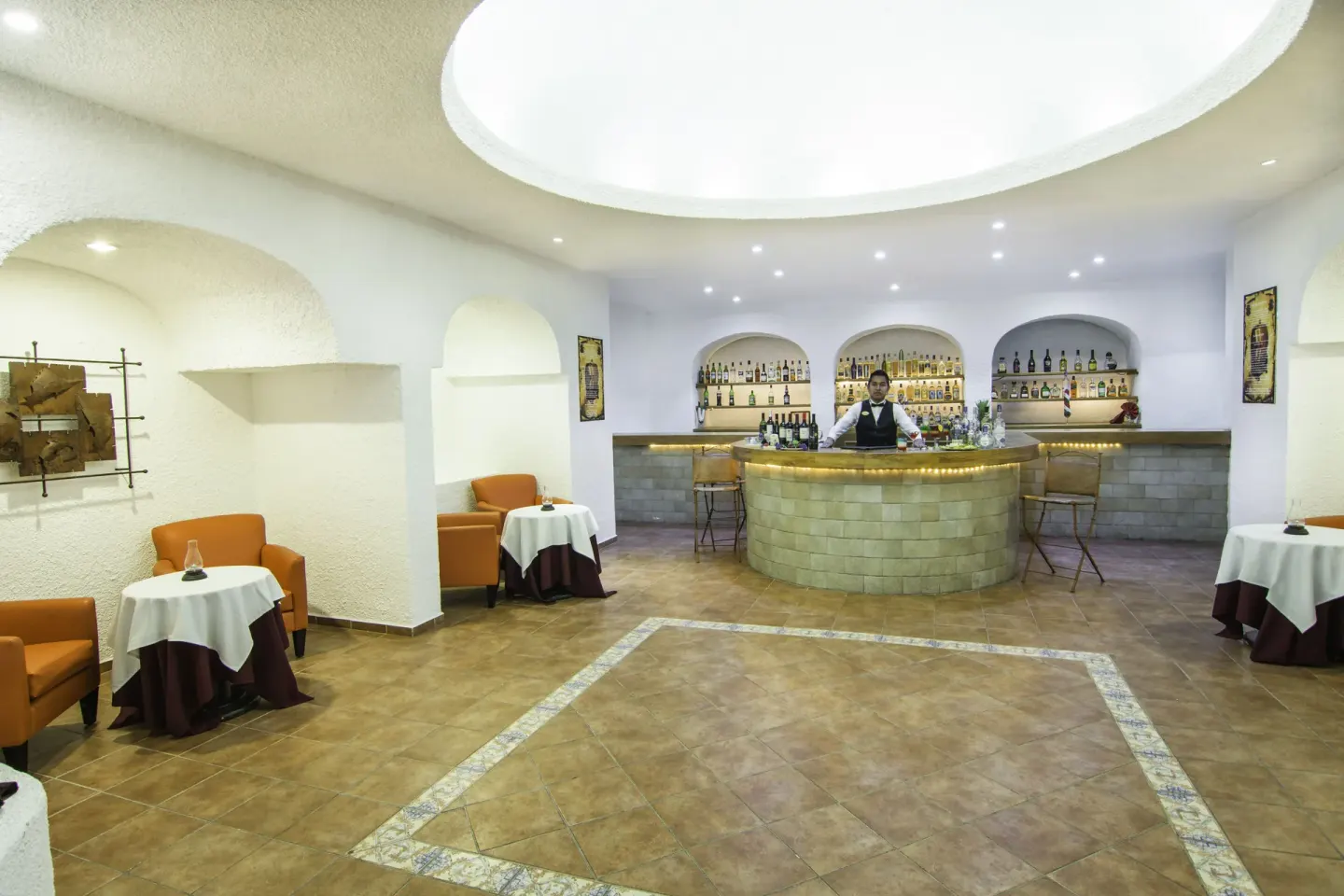 Lobby bar with curved counter, bottle shelves, and small tables at Tesoro Manzanillo.