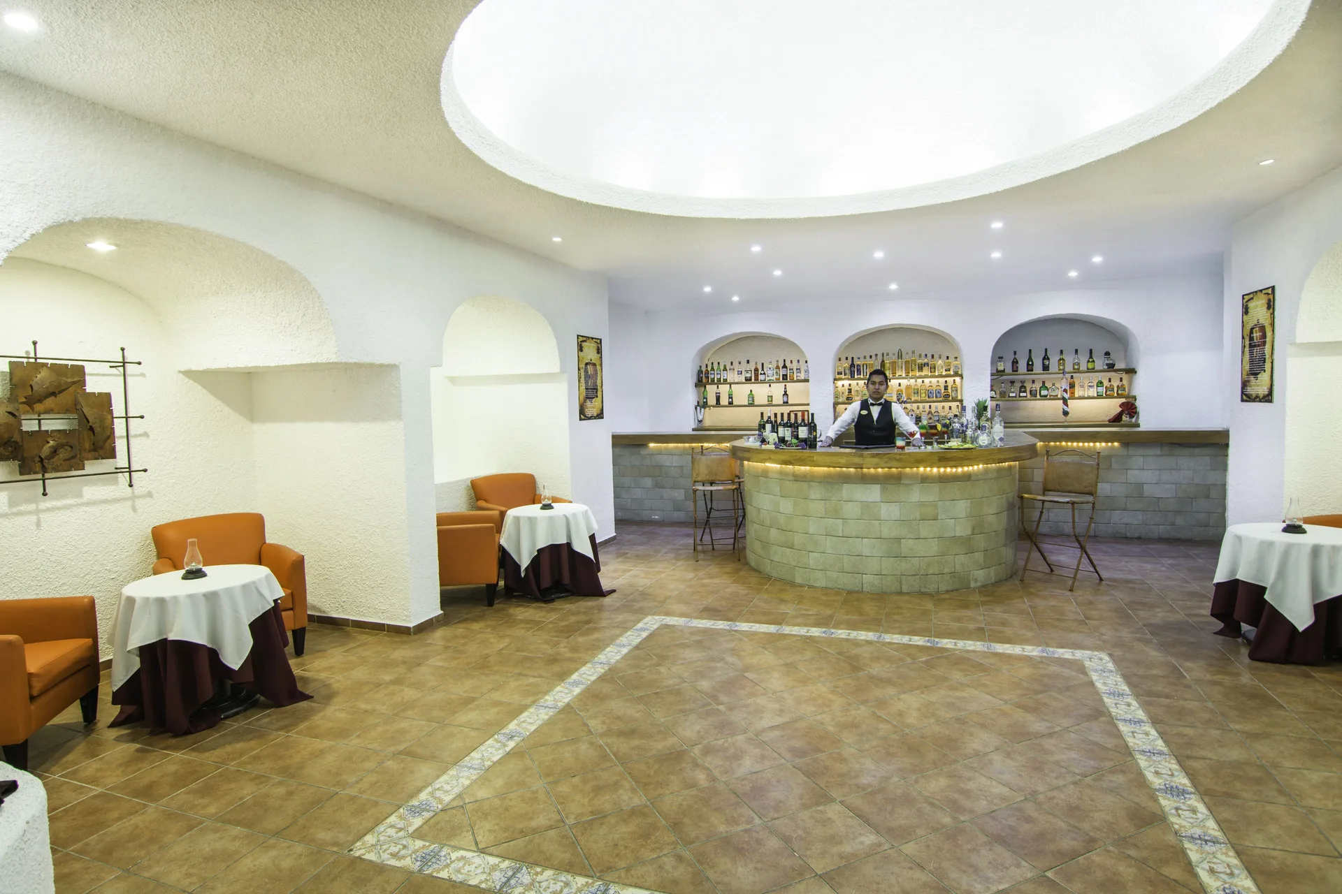 Lobby bar with curved counter, bottle shelves, and small tables at Tesoro Manzanillo.