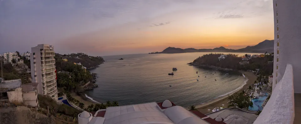 Ocean bay sunset view from Tesoro Manzanillo with beach, boats, and hills.