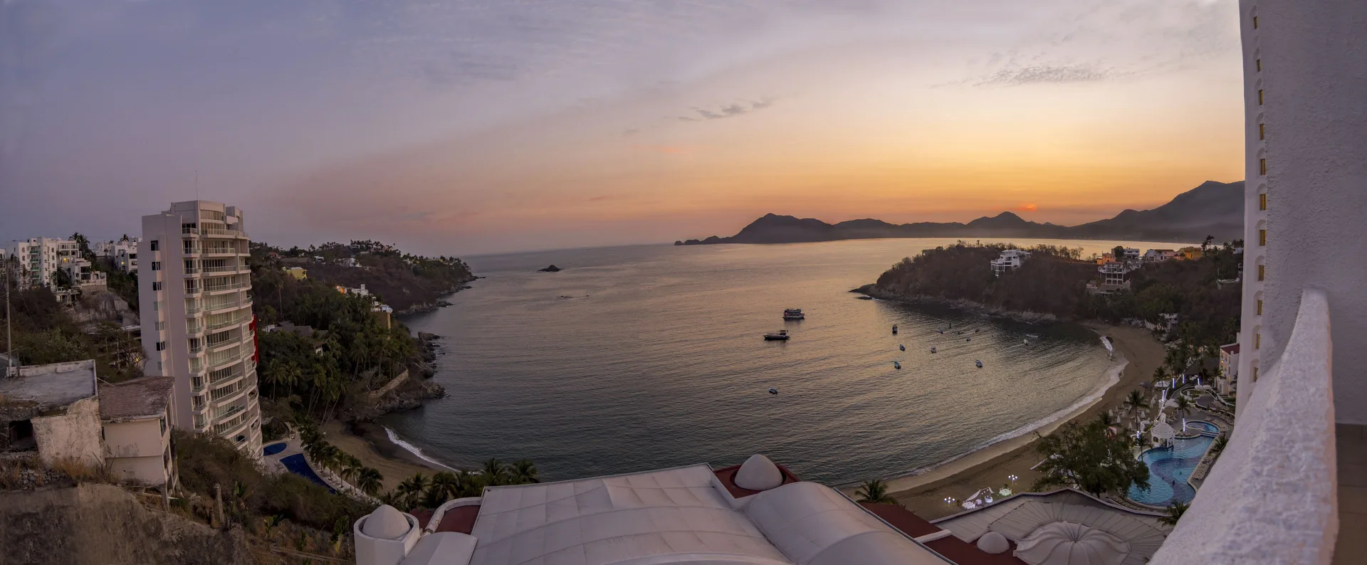 Ocean bay sunset view from Tesoro Manzanillo with beach, boats, and hills.