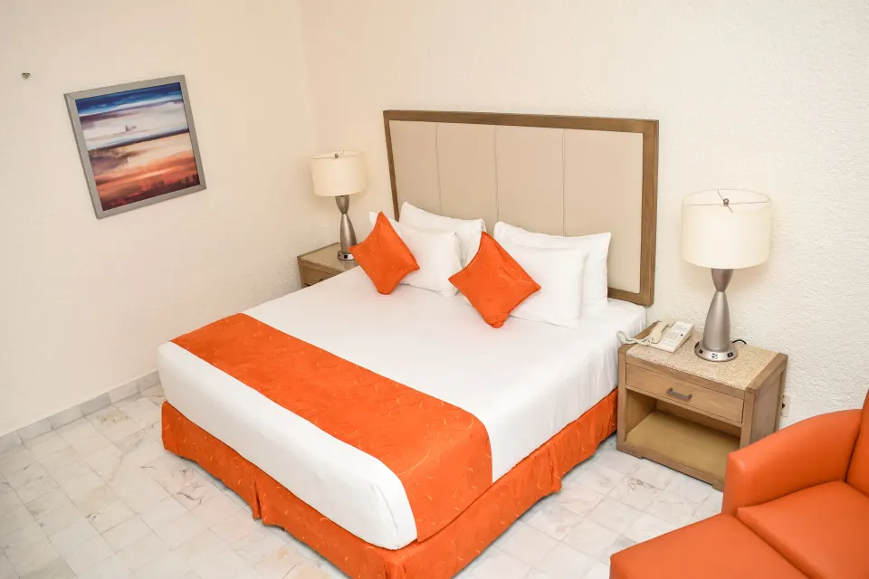 Standard Room Mountain View king bed, nightstands, wall art, and orange chair at Tesoro Manzanillo.