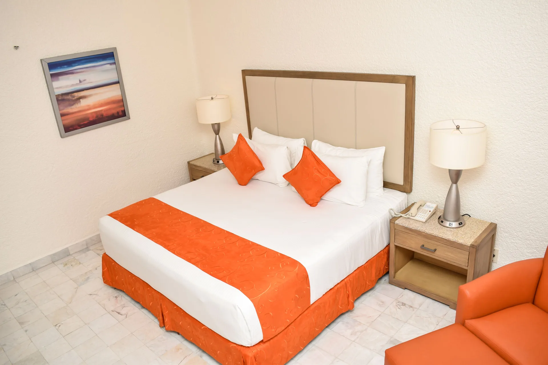Standard Room Mountain View king bed, nightstands, wall art, and orange chair at Tesoro Manzanillo.