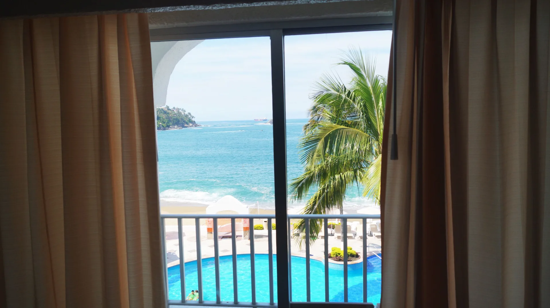 Standard Room Ocean View balcony view of pool, palm, and bay at Tesoro Manzanillo.