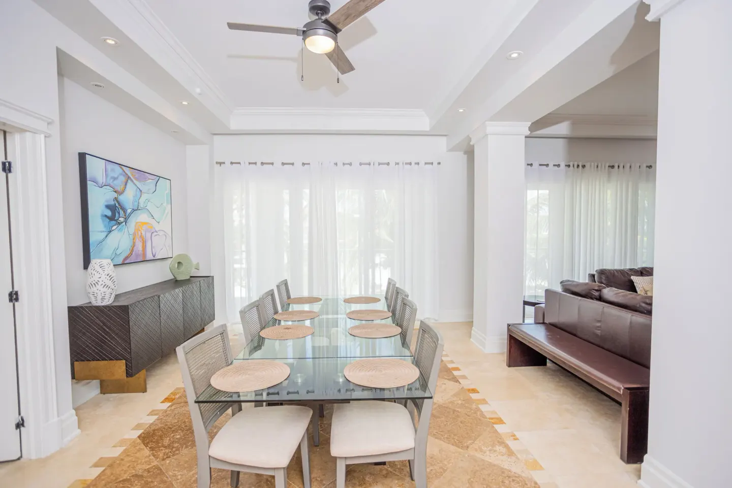 Dining area with glass table, eight chairs, sideboard, and adjoining lounge at The Atrium Resort.