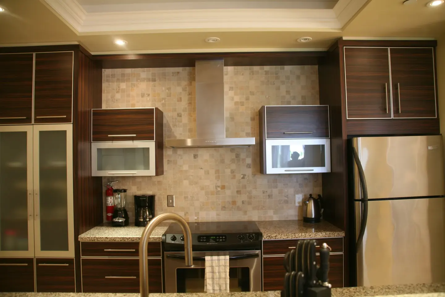Full kitchen with wood cabinetry, stainless appliances, cooktop, and island at The Atrium Resort.