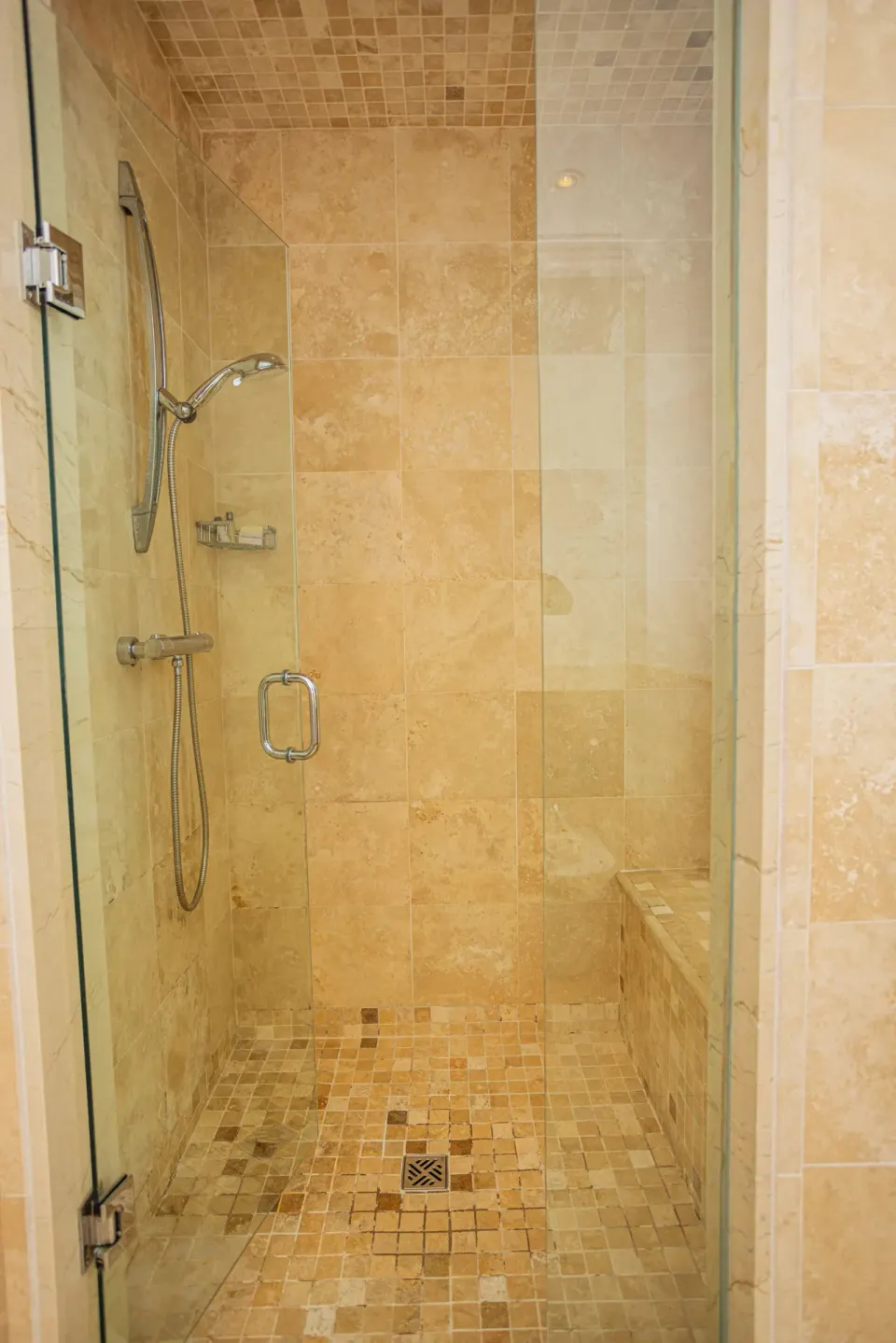 Glass walk-in shower with beige tile and bench at The Atrium Resort.