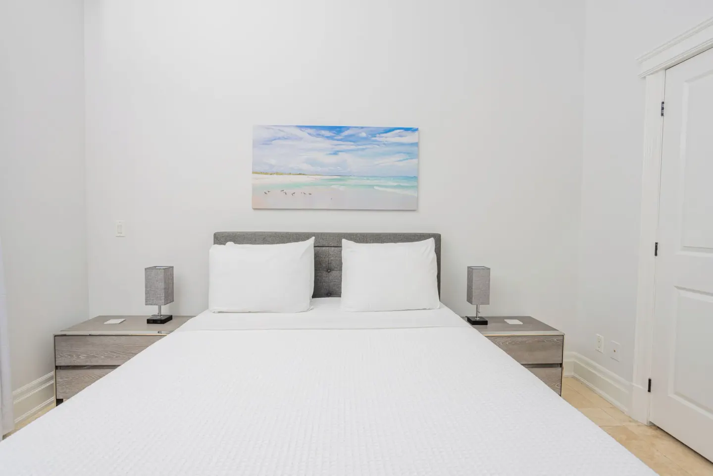 Guest bedroom with white bed and beach artwork at The Atrium Resort.