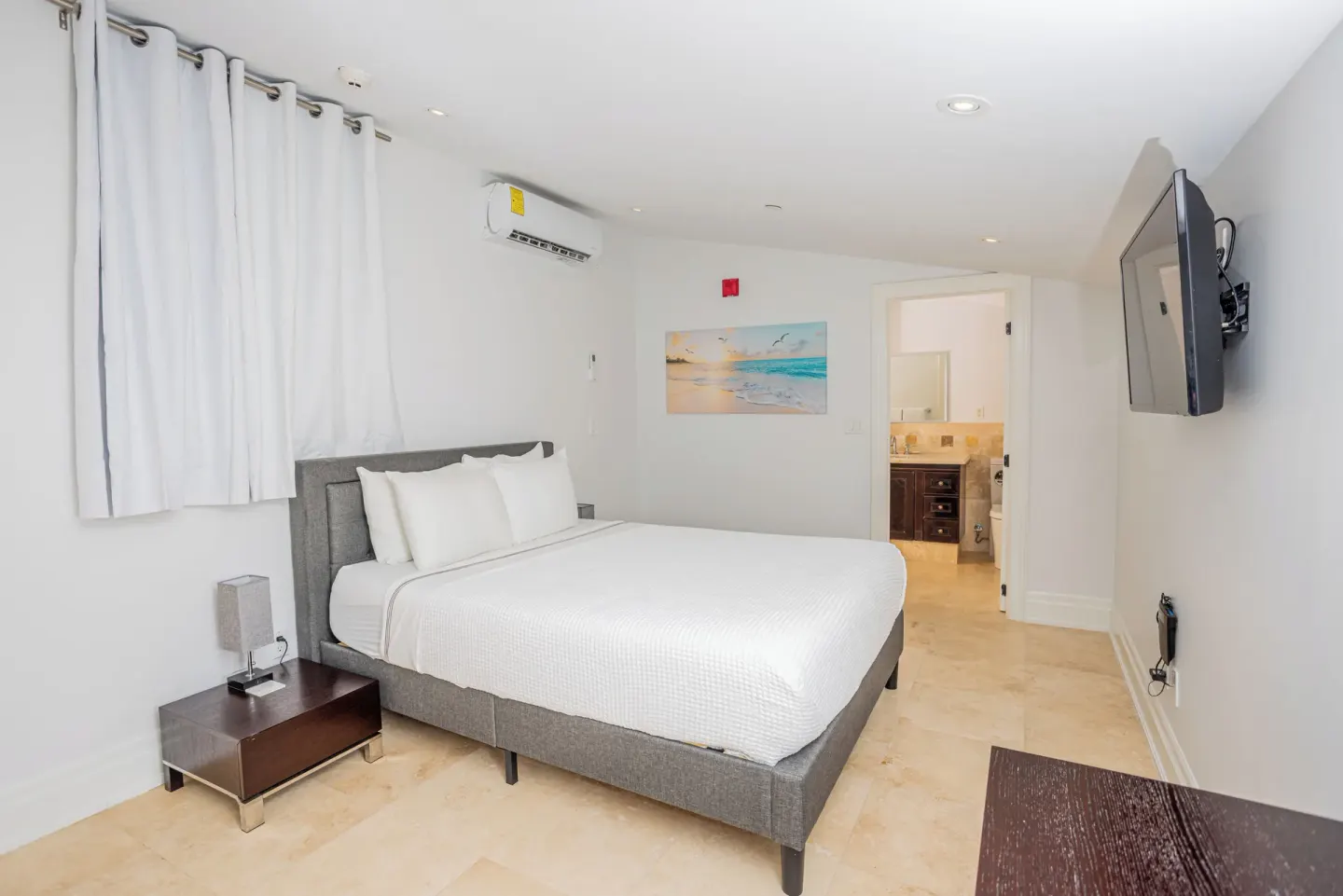 Guest room with king bed, wall TV, bathroom doorway, and white curtains at The Atrium Resort.