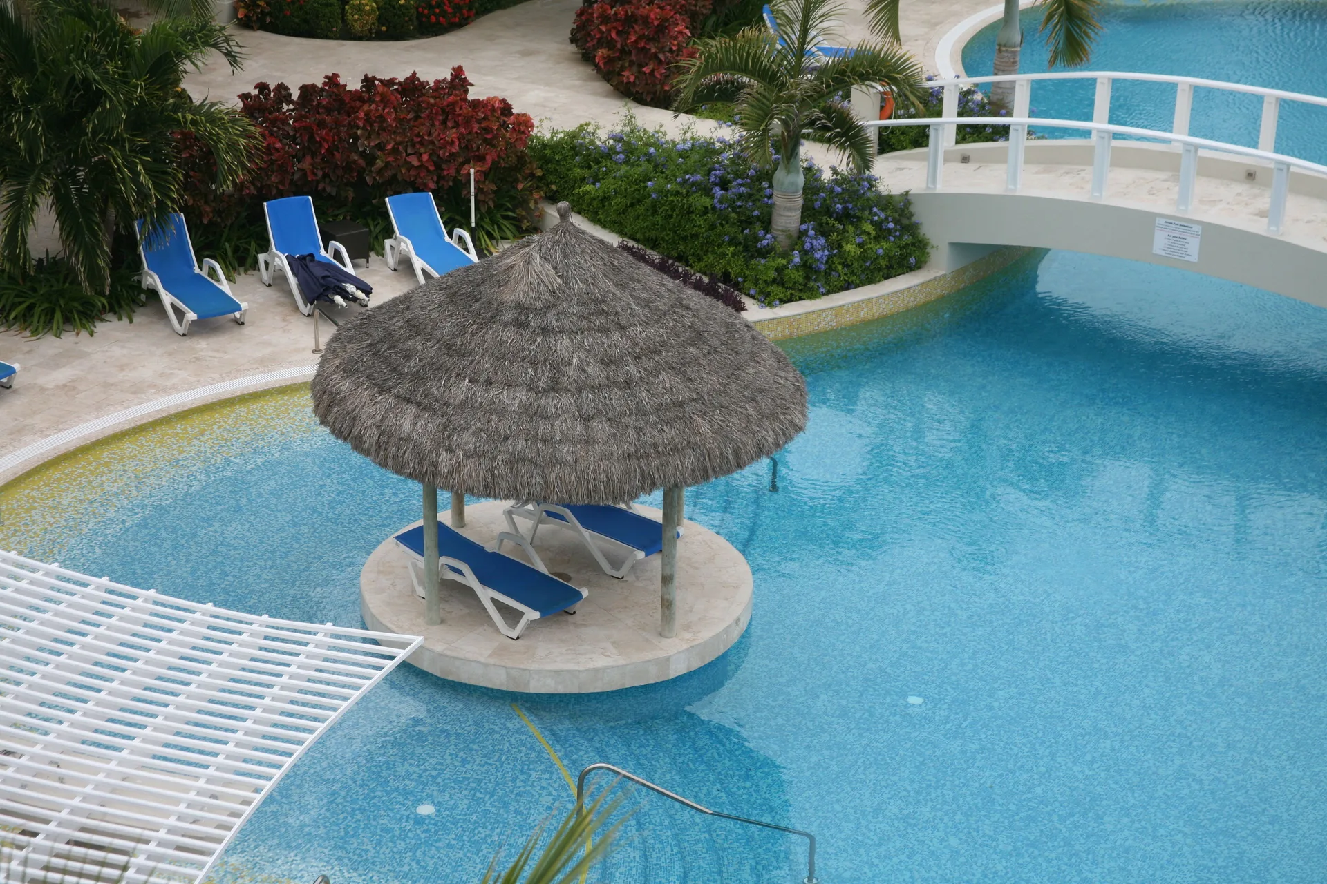 Pool island with a thatched shade roof and blue loungers at The Atrium Resort.