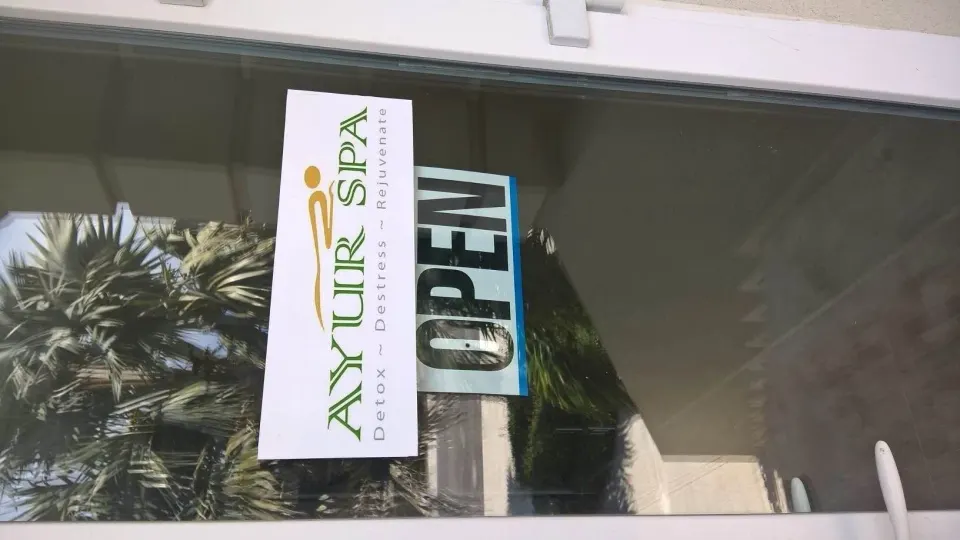 A spa entrance window with an open sign and palm reflections at The Atrium Resort.