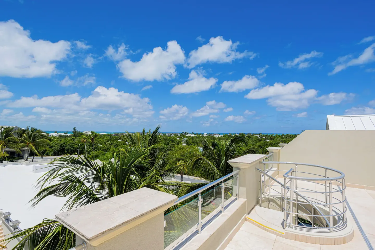 Sunny terrace with glass railing and treetop ocean view at The Atrium Resort.