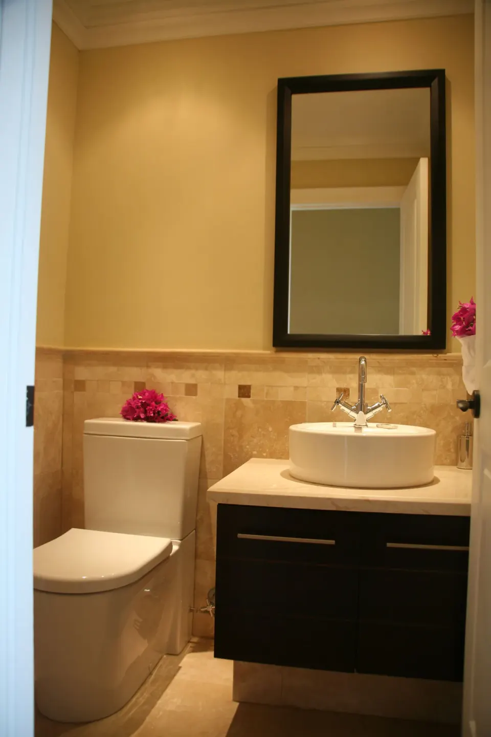 One-bedroom condo bathroom with toilet, vessel sink, mirror, and flowers at The Atrium Resort.