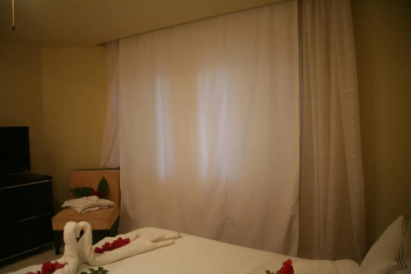 Studio sleeping area with curtained window, bed, chair, and TV at The Atrium Resort.