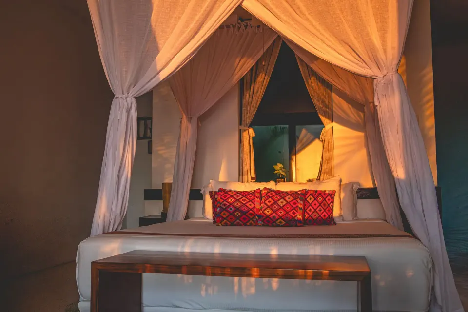 Sunlit canopy bed with decorative pillows in a guest room at The Beach Tulum