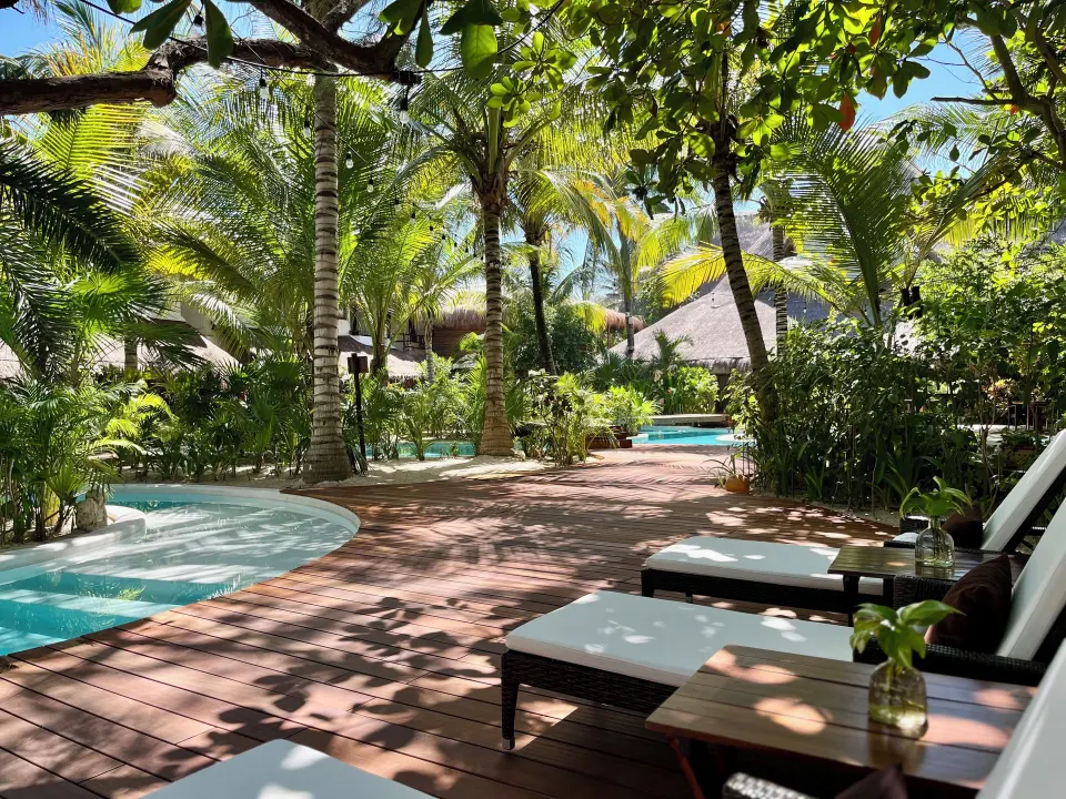 Sun-dappled wooden deck with loungers and shallow pools at The Beach Tulum