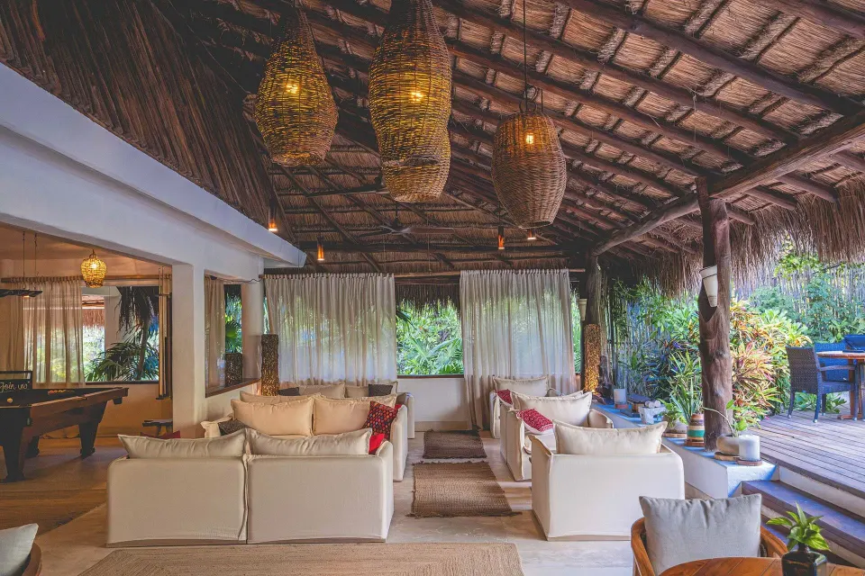Open palapa lounge with sofas, woven pendant lights and tropical views at The Beach Tulum