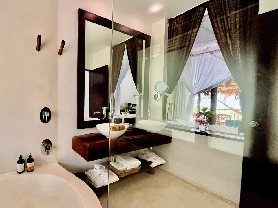 Sink and mirror with view into curtained bedroom at The Beach Tulum